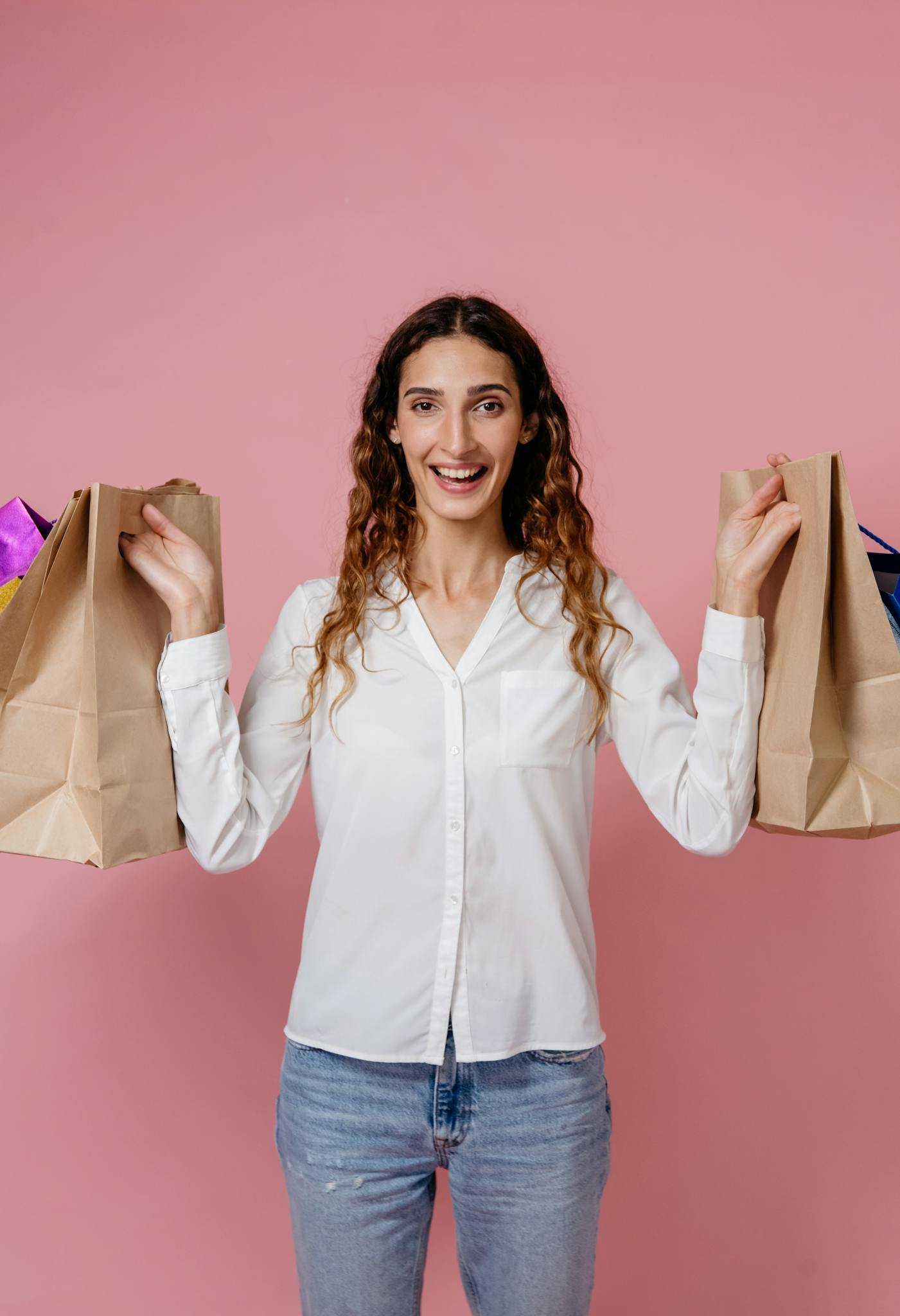 A joyful woman holding shopping bags against a pink studio background, expressing happiness and fashion.